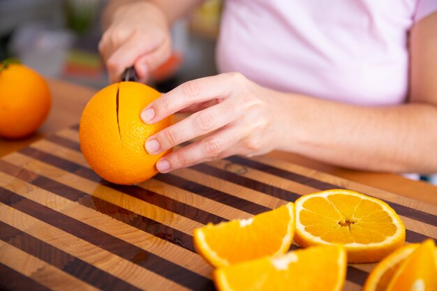 Free photo lady holding knife and cutting orange on wooden board