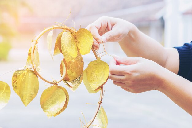 A lady is hanging the golden bo leaf wishing for happiness at Wat Phrathat Chae Haeng