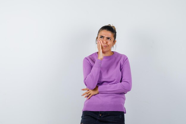 Lady keeping hand on cheek in wool blouse and looking pensive 