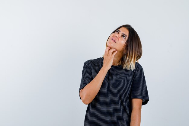 Lady keeping hand under chin in black t-shirt and looking dreamy. front view.