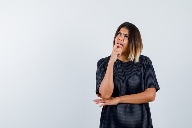 Lady keeping hand on chin in black t-shirt and looking thoughtful , front view.