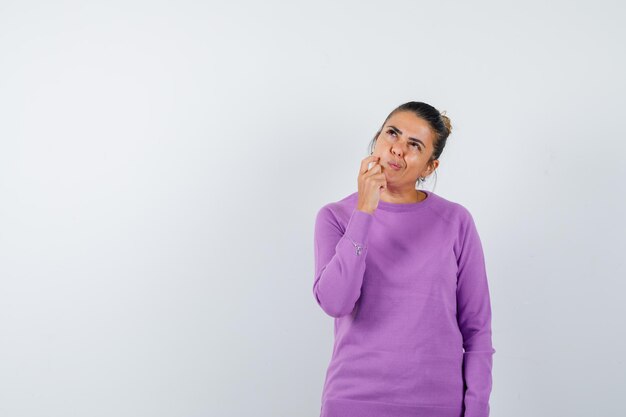 Lady keeping hand on chin in wool blouse and looking indecisive 