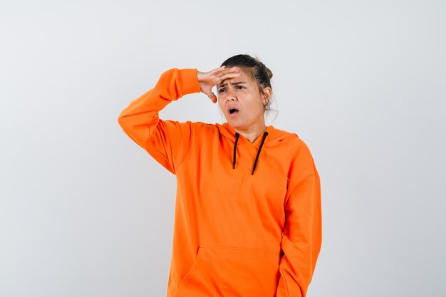 Lady keeping hand over head in orange hoodie and looking surprised