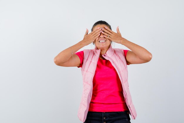 Lady keeping hands on eyes in t-shirt, vest and looking happy 