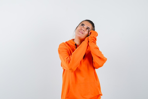 Lady leaning on palms as pillow in orange hoodie and looking dreamy