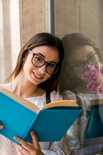 Lady looking at camera and holding book near window