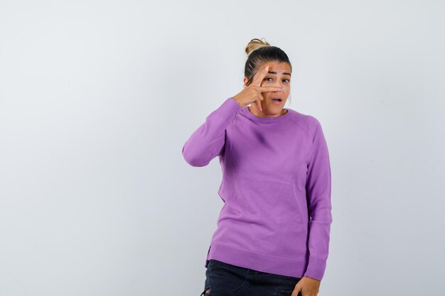 Lady looking through fingers in wool blouse and looking curious 