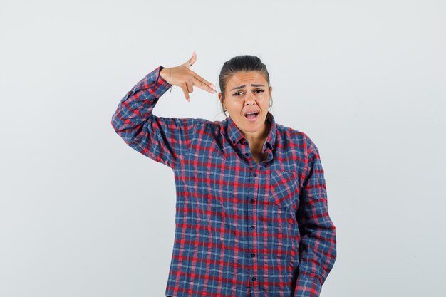 Lady making suicide gesture in casual shirt and looking mournful. front view.