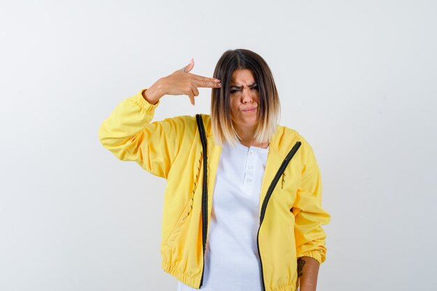 Lady making suicide gesture in t-shirt, jacket and looking spiteful. front view.