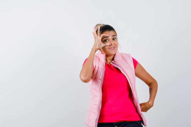 Lady opening eyes with fingers in t-shirt, vest and looking curious 