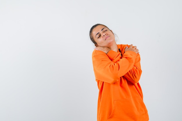 Lady in orange hoodie hugging herself while posing and looking relaxed