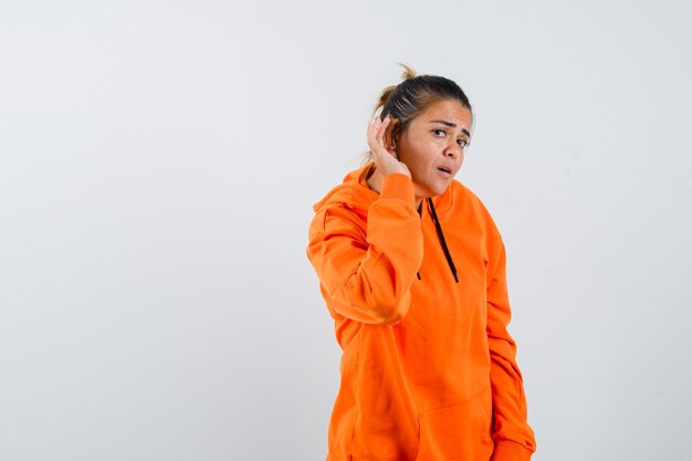 Lady in orange hoodie overhearing private conversation and looking curious