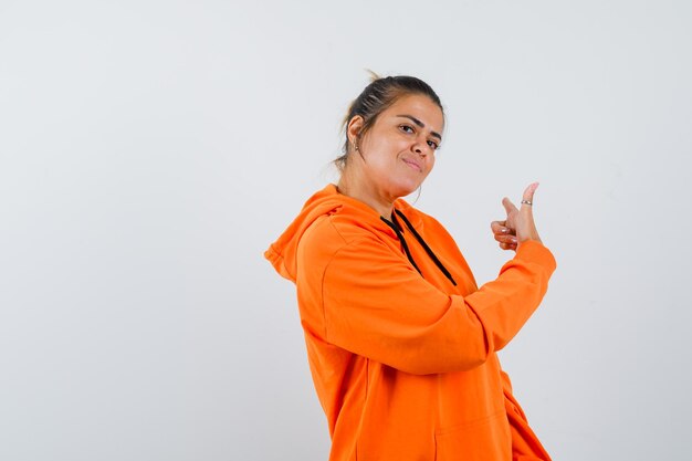 Lady in orange hoodie pointing away and looking confident