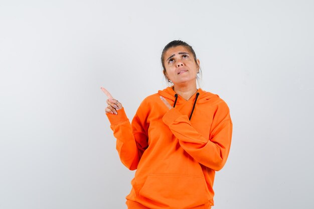 Lady in orange hoodie pointing at upper left corner and looking pensive