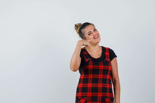 Lady in pinafore dress pointing at her teeth and looking cheery , front view.