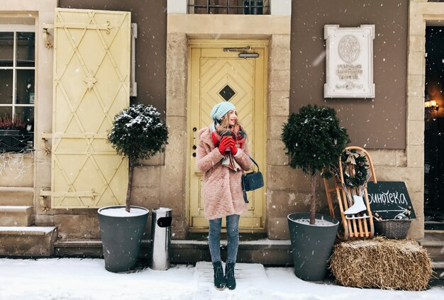 雪の中の木製のドアの前にピンクのコートの女性が立つ