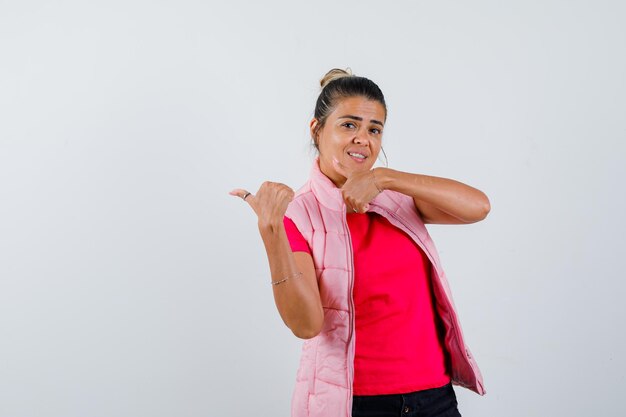 Lady pointing aside with thumbs in t-shirt, vest and looking confident 