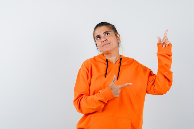 Lady pointing fingers up and to the side in orange hoodie and looking dreamy