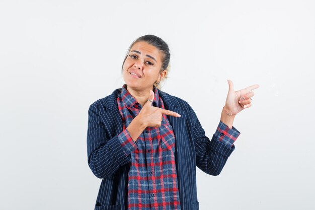 Lady pointing to the right side in shirt, jacket and looking confident. front view.