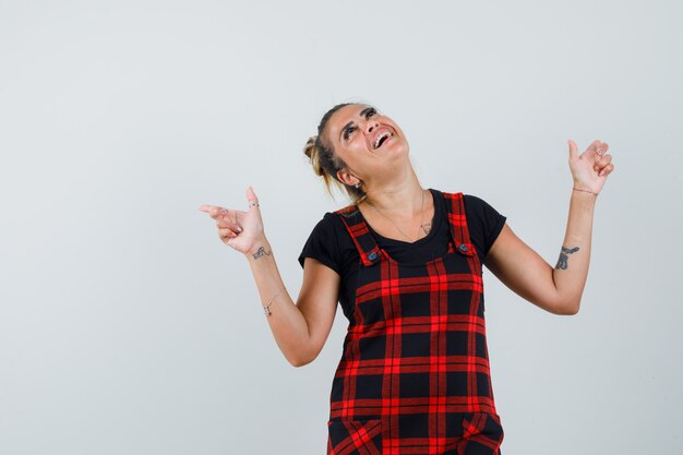 Lady pointing up in pinafore dress and looking happy , front view.