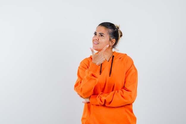 Lady pointing at upper right corner in orange hoodie and looking merry