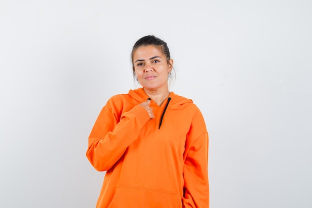 Lady posing with hand on chest in orange hoodie and looking delicate