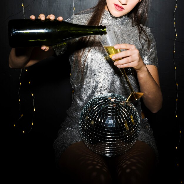 女性、ディスコのボールの近くのガラスにシャンパンを注ぐ