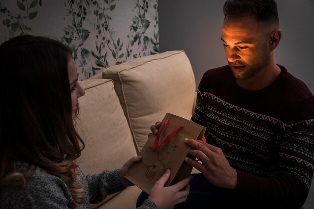 Lady presenting gift packet to guy on settee