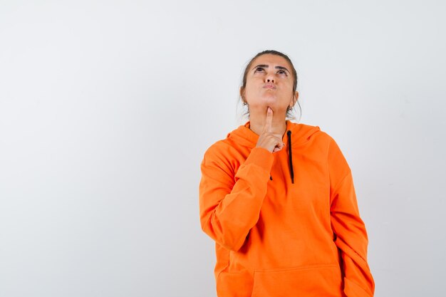 Lady propping chin on finger in orange hoodie and looking pensive