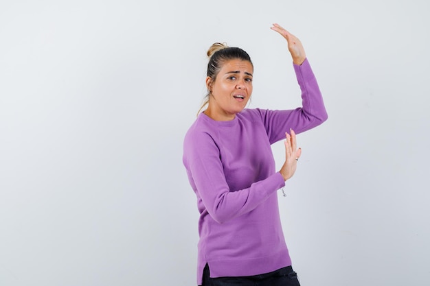 Lady raising hands to defend herself in wool blouse and looking excited 