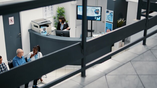 Lady receptionist working at hospital reception desk to help patients with medical appointment. Healthcare employee in waiting room lobby, checkup visit report with medication.