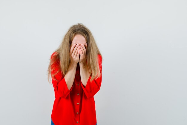 Free photo lady in red shirt covering face with hands and looking upset ,