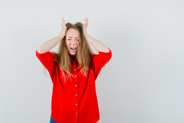 Lady in red shirt holding hands to head and looking wistful ,