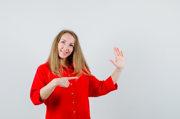 Lady in red shirt pointing aside, showing palm and looking cheery ,