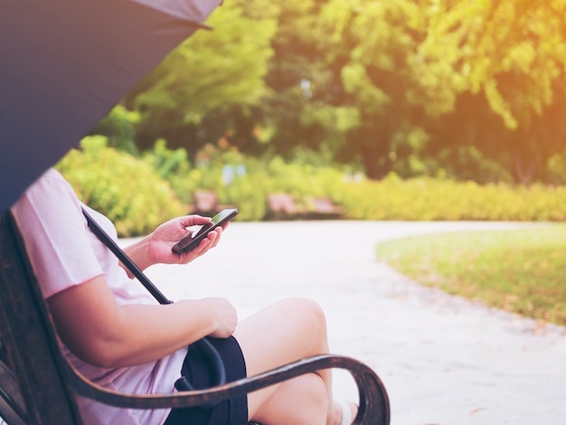 Signora rilassarsi seduti nel parco con l'ombrello e l'utilizzo del telefono cellulare
