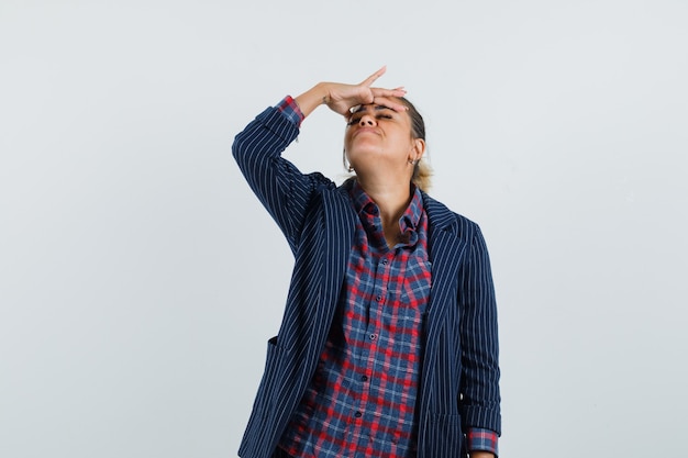 Lady rubbing her forehead in shirt, jacket and looking relaxed , front view.