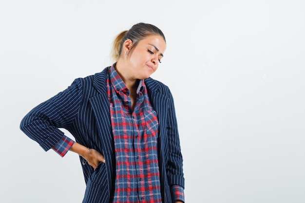 Lady in shirt, jacket having backache and looking fatigued , front view.