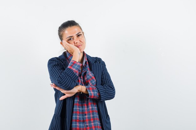 Lady in shirt, jacket holding hand on cheek and looking pensive , front view.