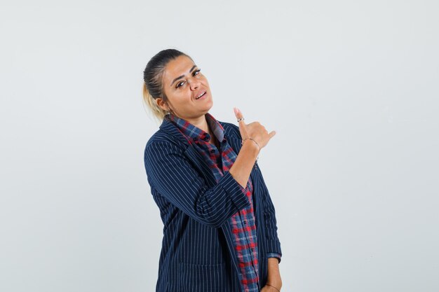 Lady in shirt, jacket showing phone gesture and looking confident , front view.