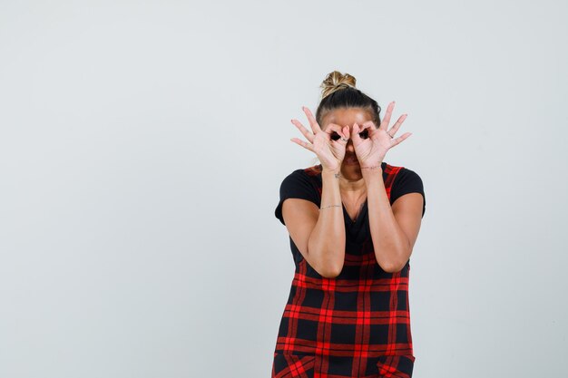 Lady showing glasses gesture in pinafore dress and looking focused. front view.