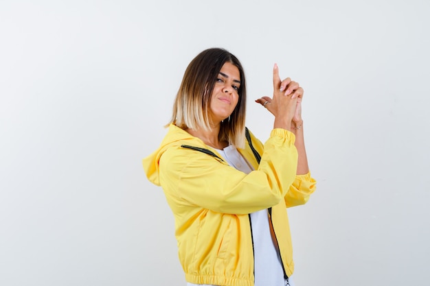 Lady showing gun gesture in t-shirt, jacket and looking confident , front view.