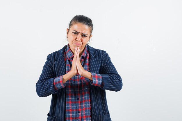 Lady showing namaste gesture in shirt, jacket and looking hopeful , front view.