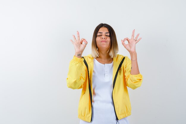 Lady showing ok gesture in t-shirt, jacket and looking relaxed. front view.