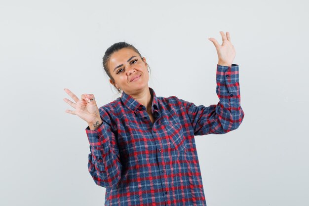 Lady showing ok sign, raising hand in casual shirt and looking confident. front view.