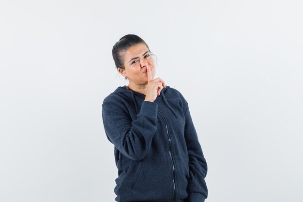 Lady showing silence gesture in hoodie and looking confident. front view.