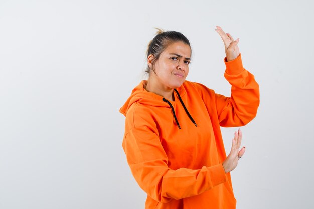 Lady showing stop gesture in orange hoodie and looking scared