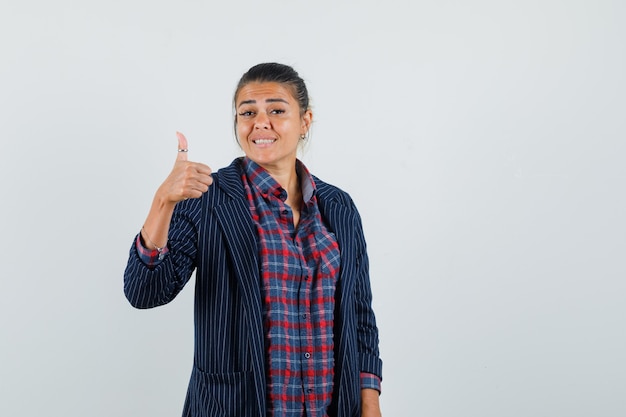 Lady showing thumb up in shirt, jacket and looking glad , front view.