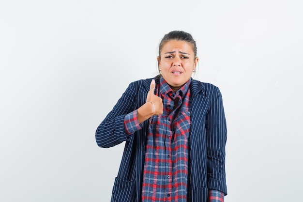 Lady showing thumb up in shirt, jacket and looking mournful , front view.