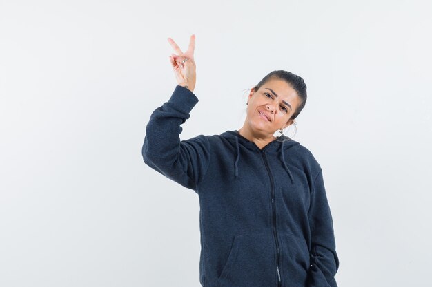 Lady showing victory gesture in hoodie and looking lucky. front view.