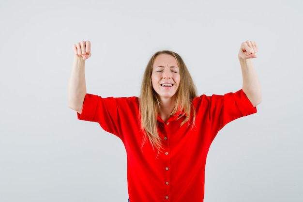 Lady showing winner gesture in red shirt and looking blissful.